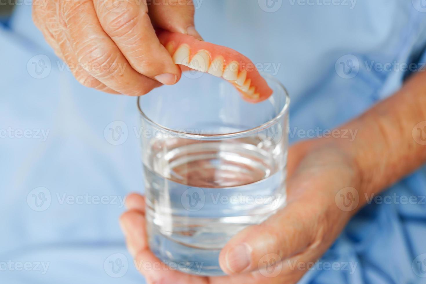 Asian senior woman patient clean teeth denture in a glass with solution for chew food. photo