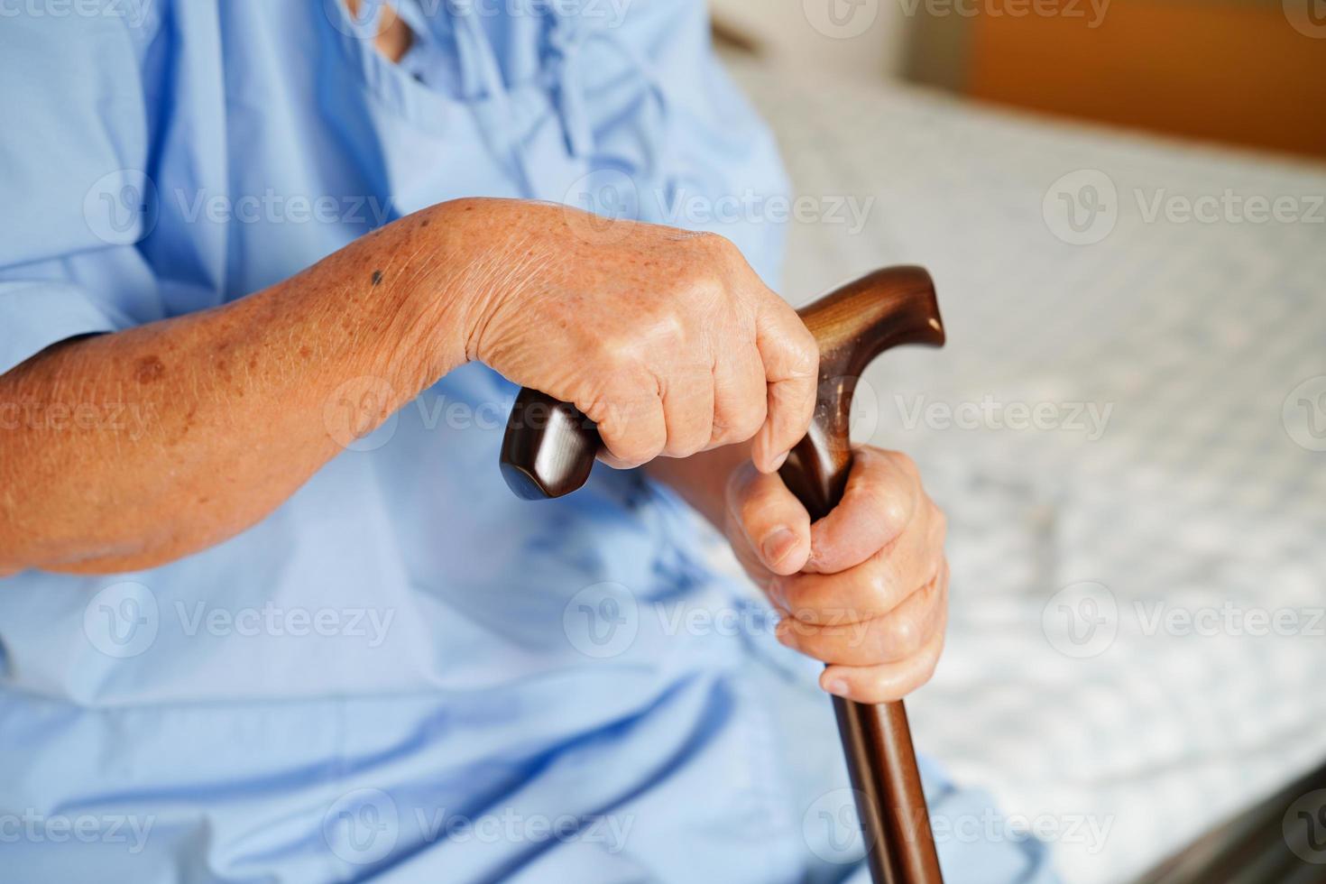 Asian elderly disability woman patient holding walking stick in wrinkled hand at hospital. photo