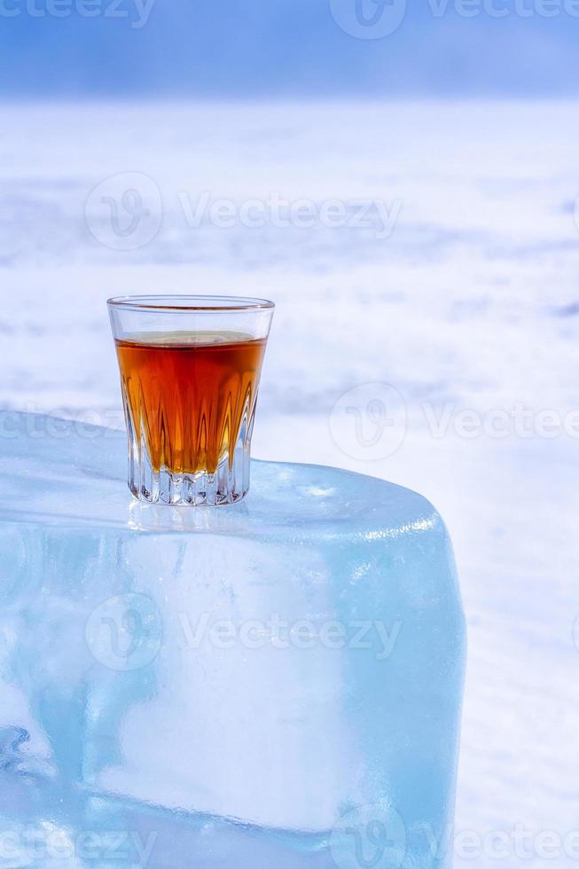 Whiskey in a glass stands on an ice block. Orange alcoholic drink in a
