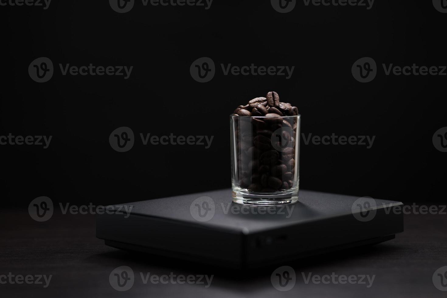 Dark roasted coffee beans in a clear glass on a black digital scale. photo