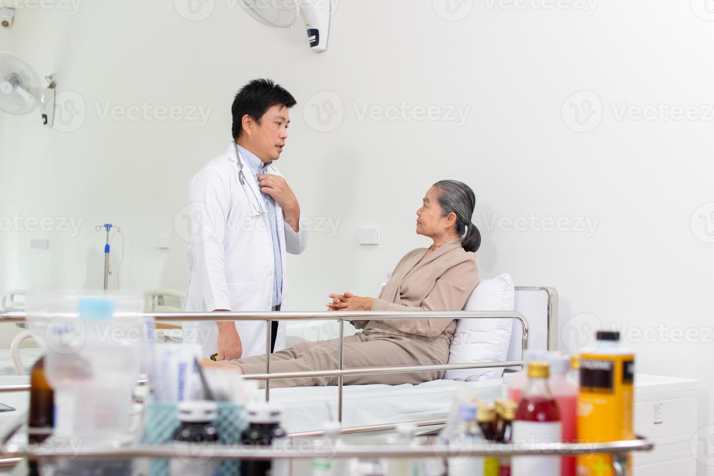 Asian male doctor explaining medicine to elderly female patient in hospital. photo