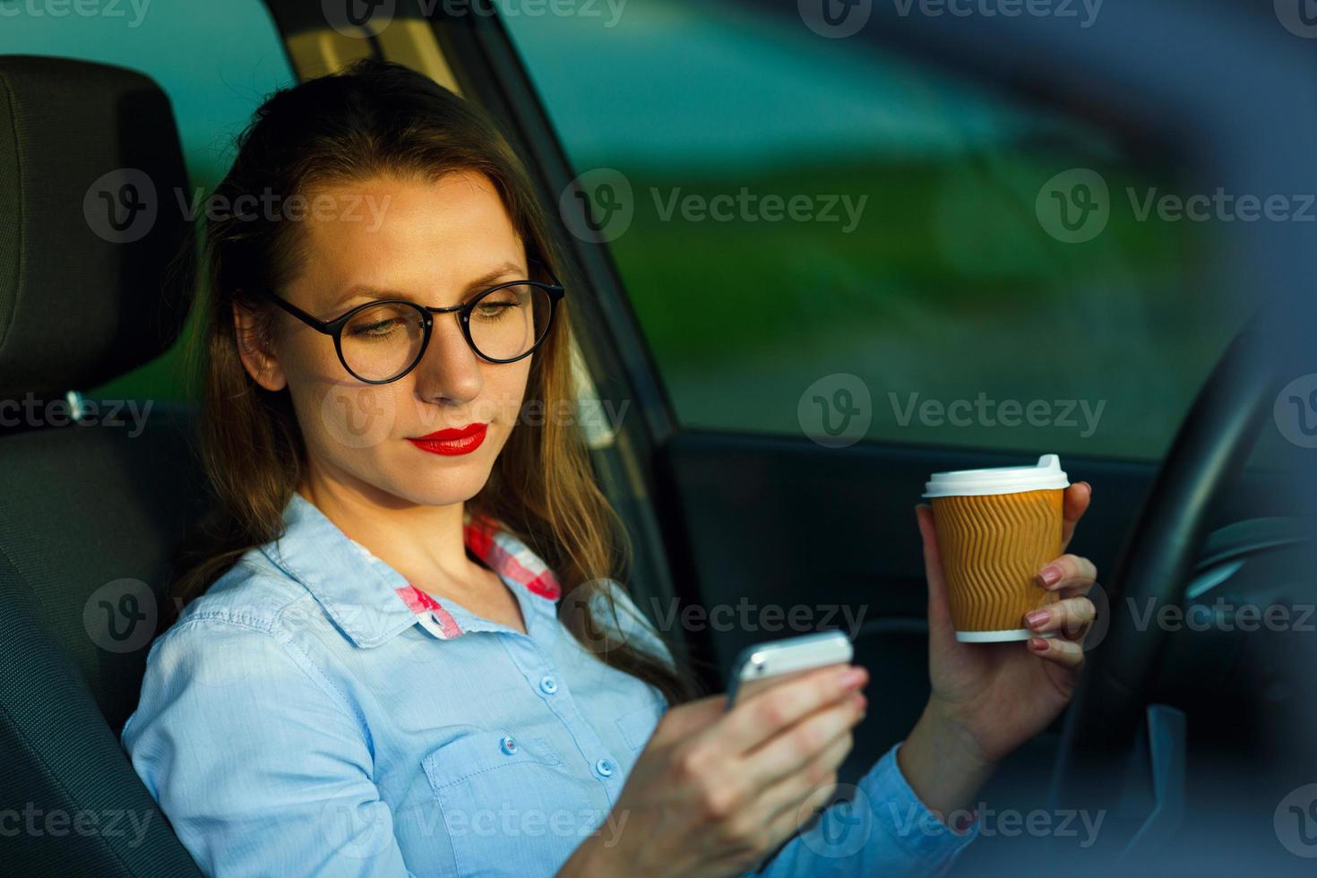 Businesswoman sending a text message and drinking coffee while driving a car photo