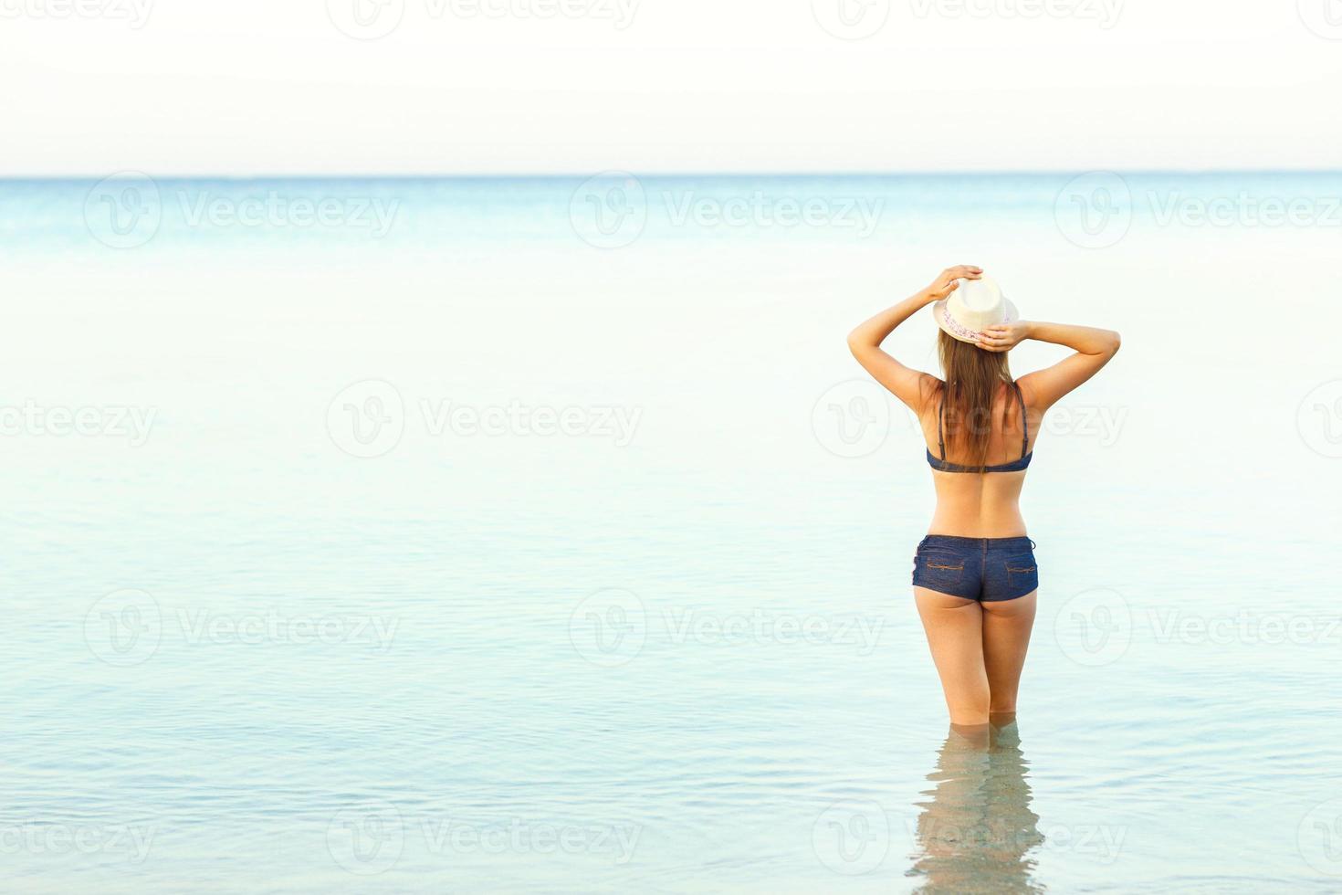 Woman in sun hat and bikini enjoying looking view of beach on hot summer day photo