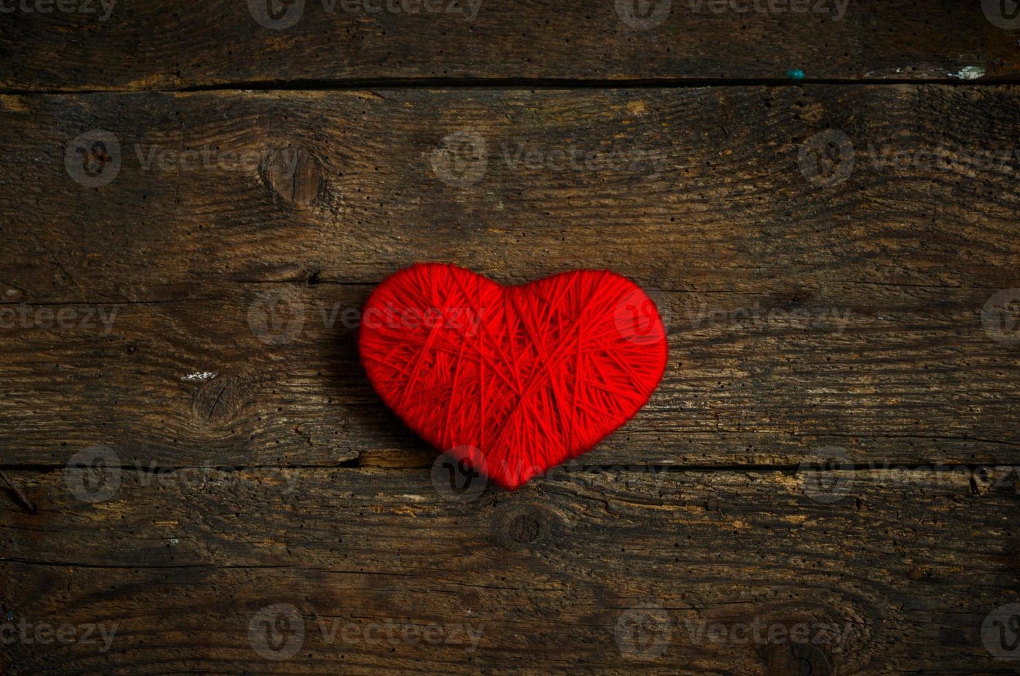 Red heart shape made from wool on old shabby wooden background photo