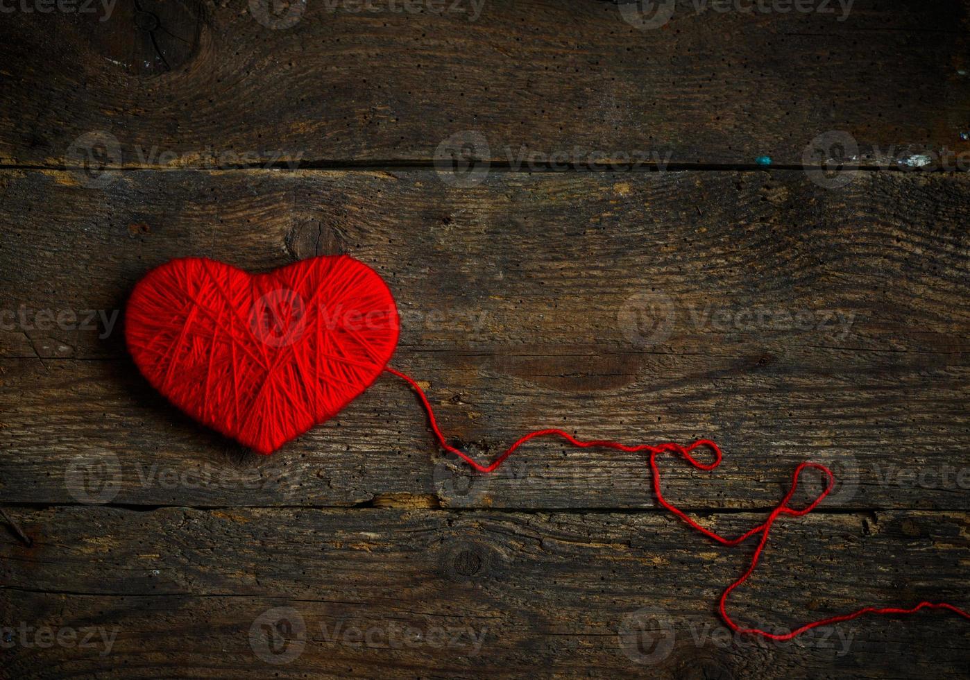 Red heart shape made from wool on old shabby wooden background photo