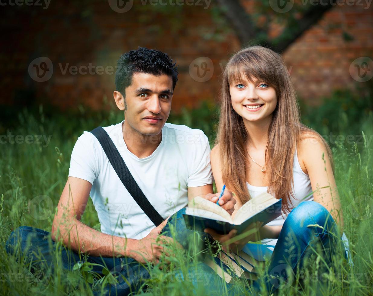Two students studying in park on grass with book outdoors photo