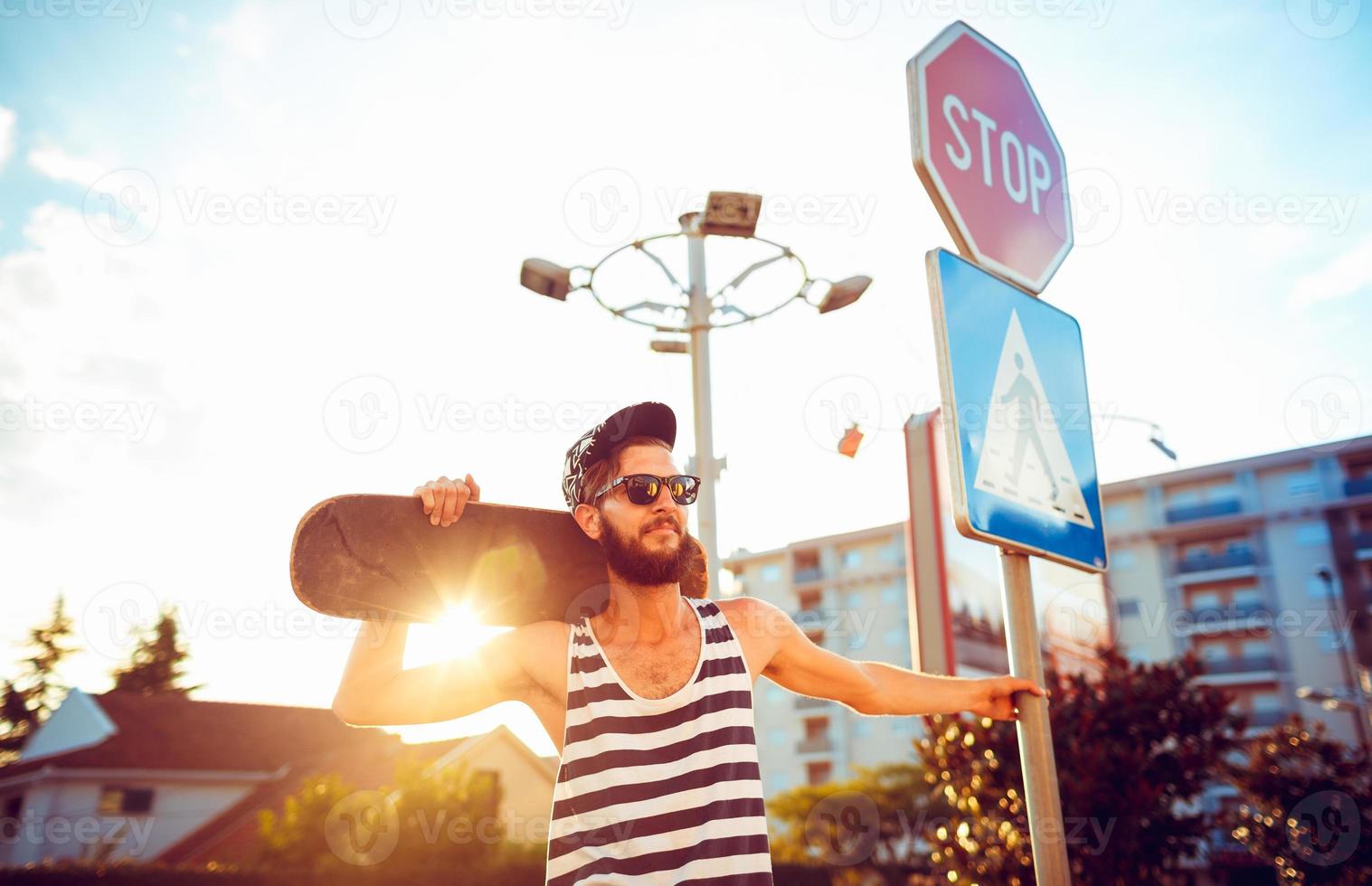 Stylish man in sunglasses with a skateboard on a street in the city at sunset light photo