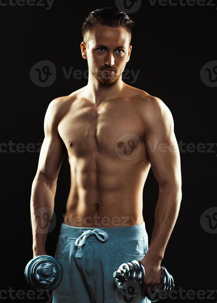 Athletic man with dumbbells on the black background photo