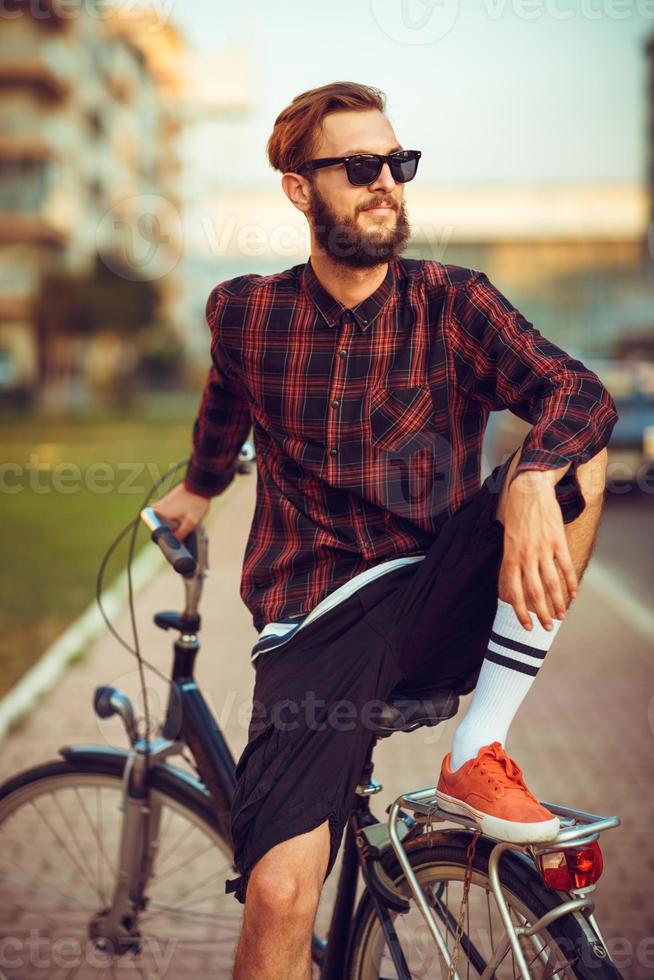 elegante hombre en Gafas de sol montando un bicicleta en ciudad calle foto
