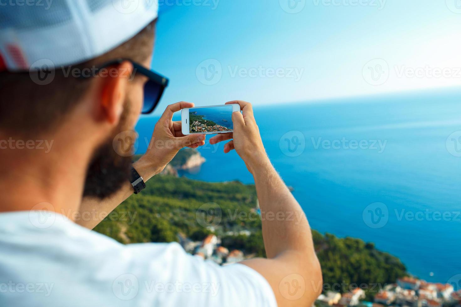 Man makes photos by a smartphone on the background of sea coast, Adriatic sea