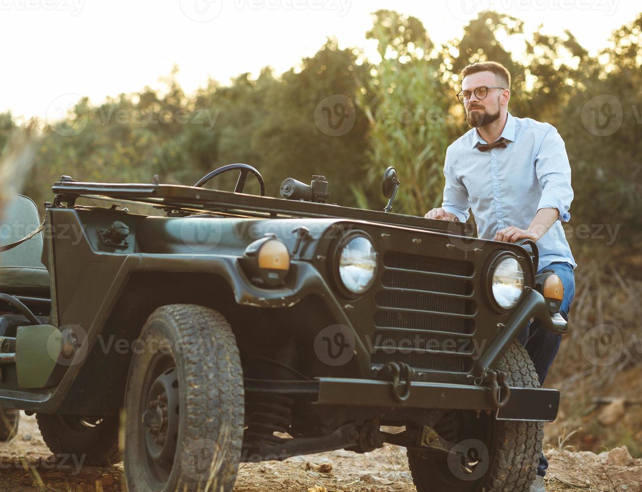 Young stylish man with glasses and bow tie near the old-fashioned SUV photo