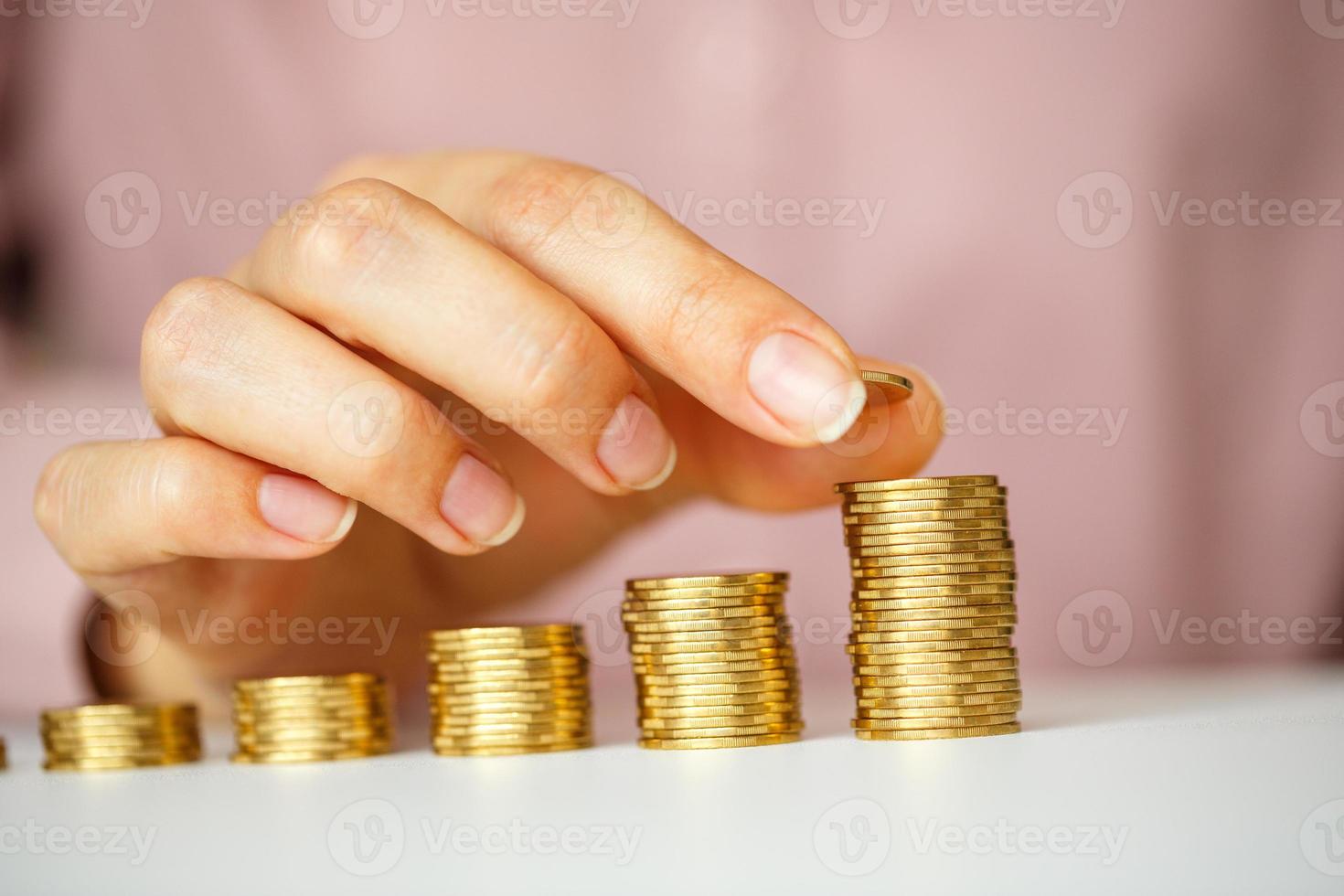 Female hand stacking gold coins into increasing columns photo