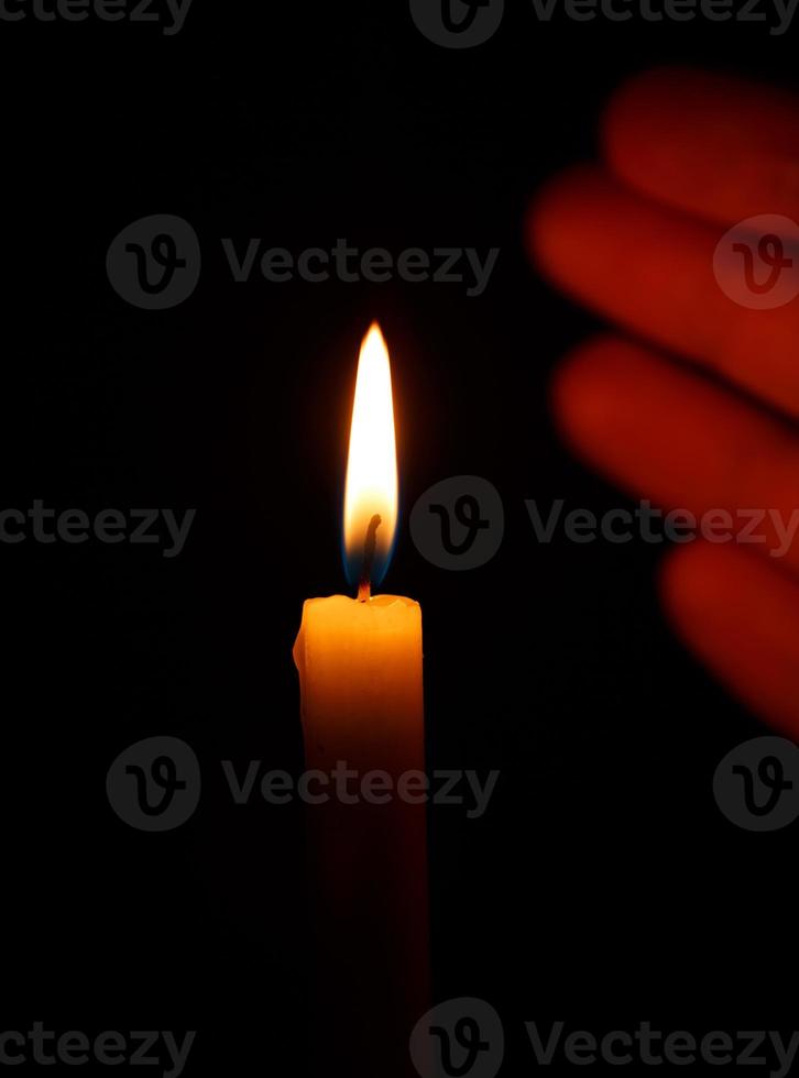 Hand protects the flame of a burning candle on a black photo