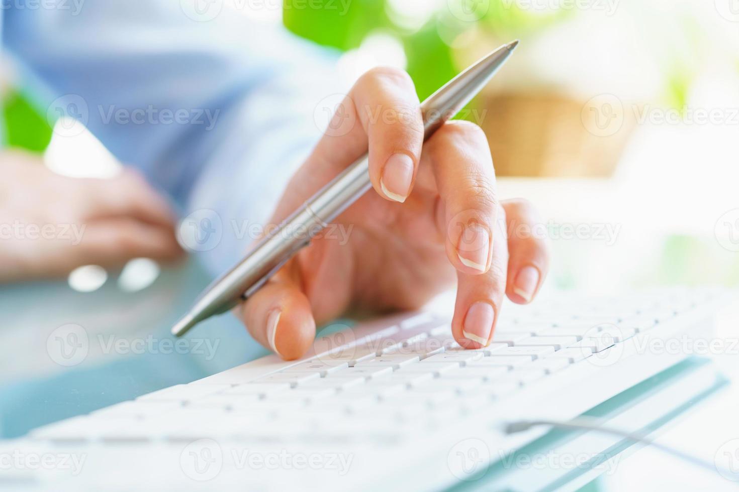 Woman office worker with pen in hand typing on the keyboard photo
