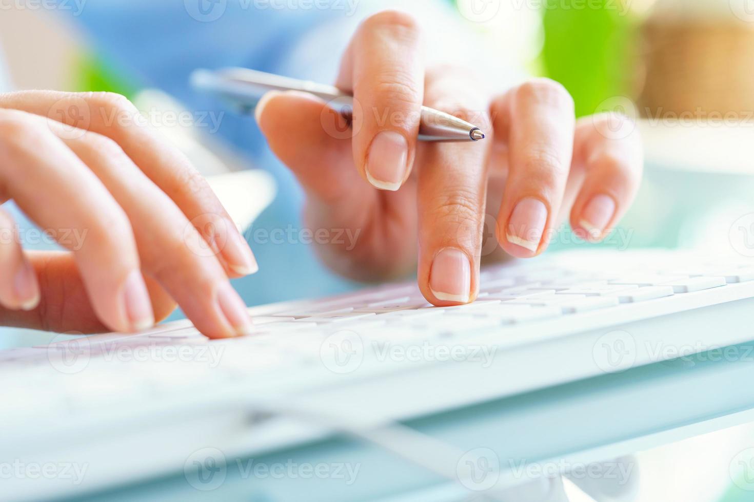 Woman office worker with pen in hand typing on the keyboard photo
