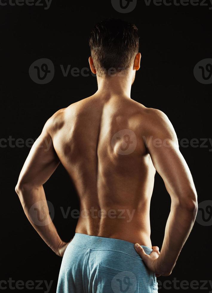 Athletic man showing his back on the black background photo