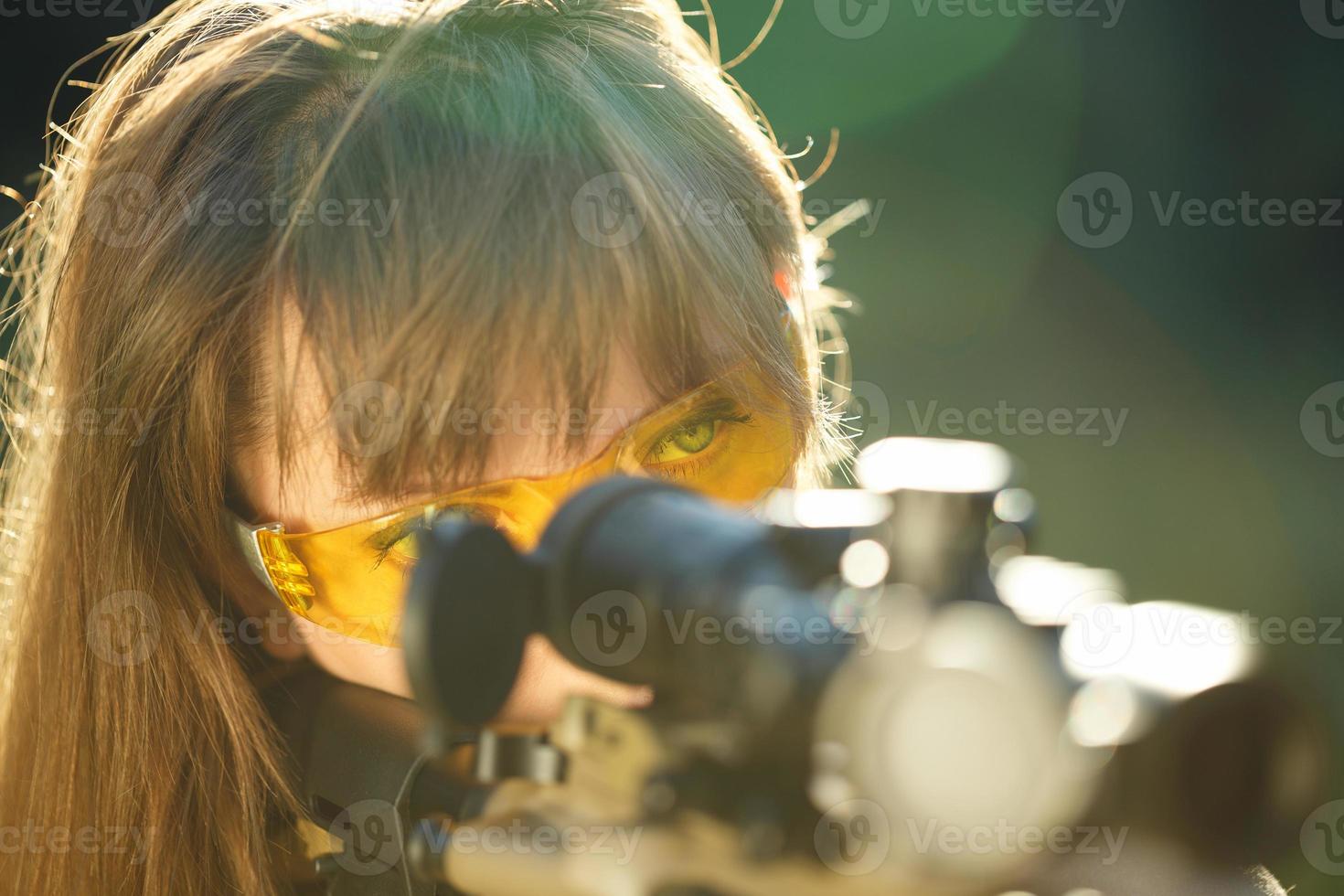 Girl with a gun for trap shooting and shooting glasses aiming at a target photo