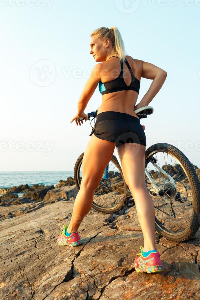 Happy athletic woman standing on the rocks with a bicycle and enjoy the view photo