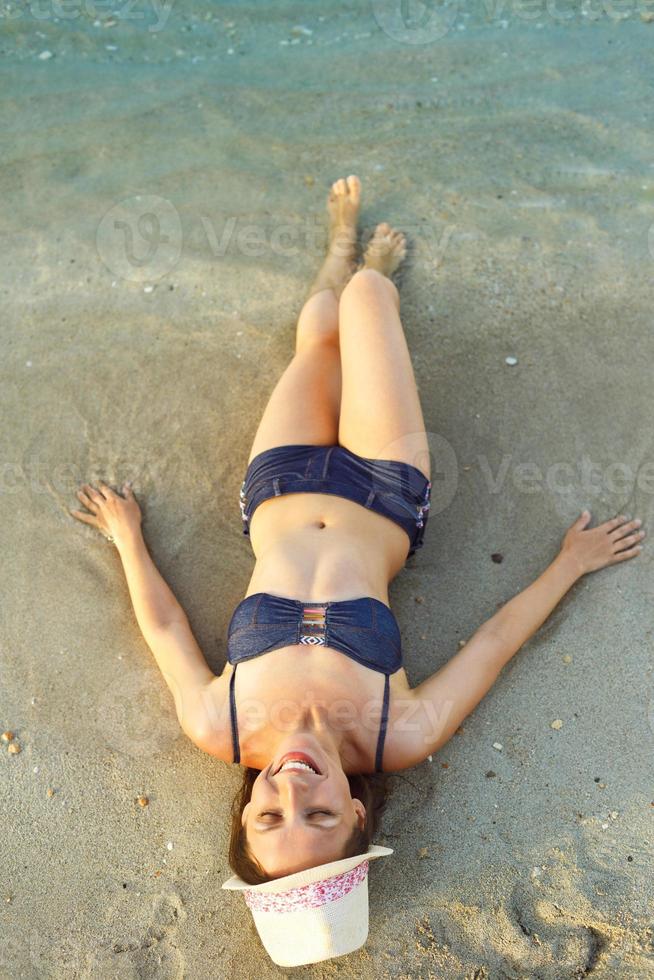 mujer en un sombrero y bikini acostado en el playa en caliente verano día foto