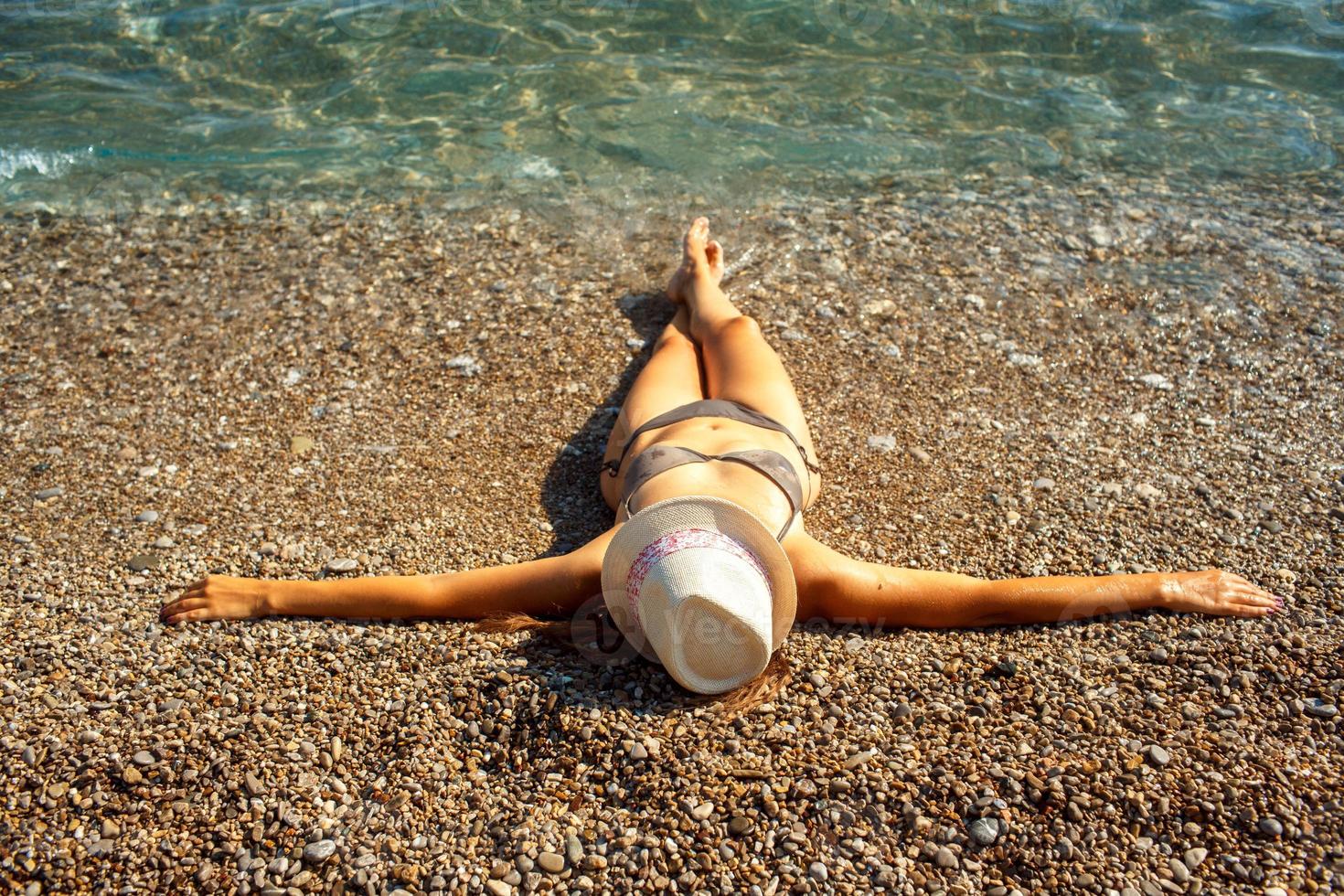 joven mujer en un sombrero y bikini acostado en el playa en caliente verano día foto