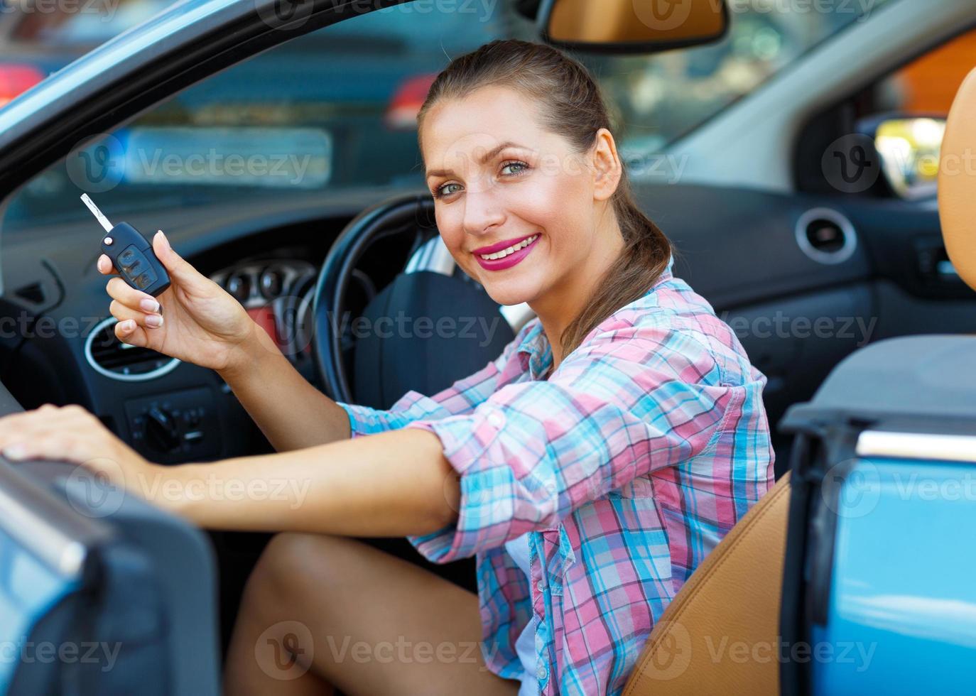 Young  woman sitting in a convertible car with the keys in hand - concept of buying a used car or a rental car photo