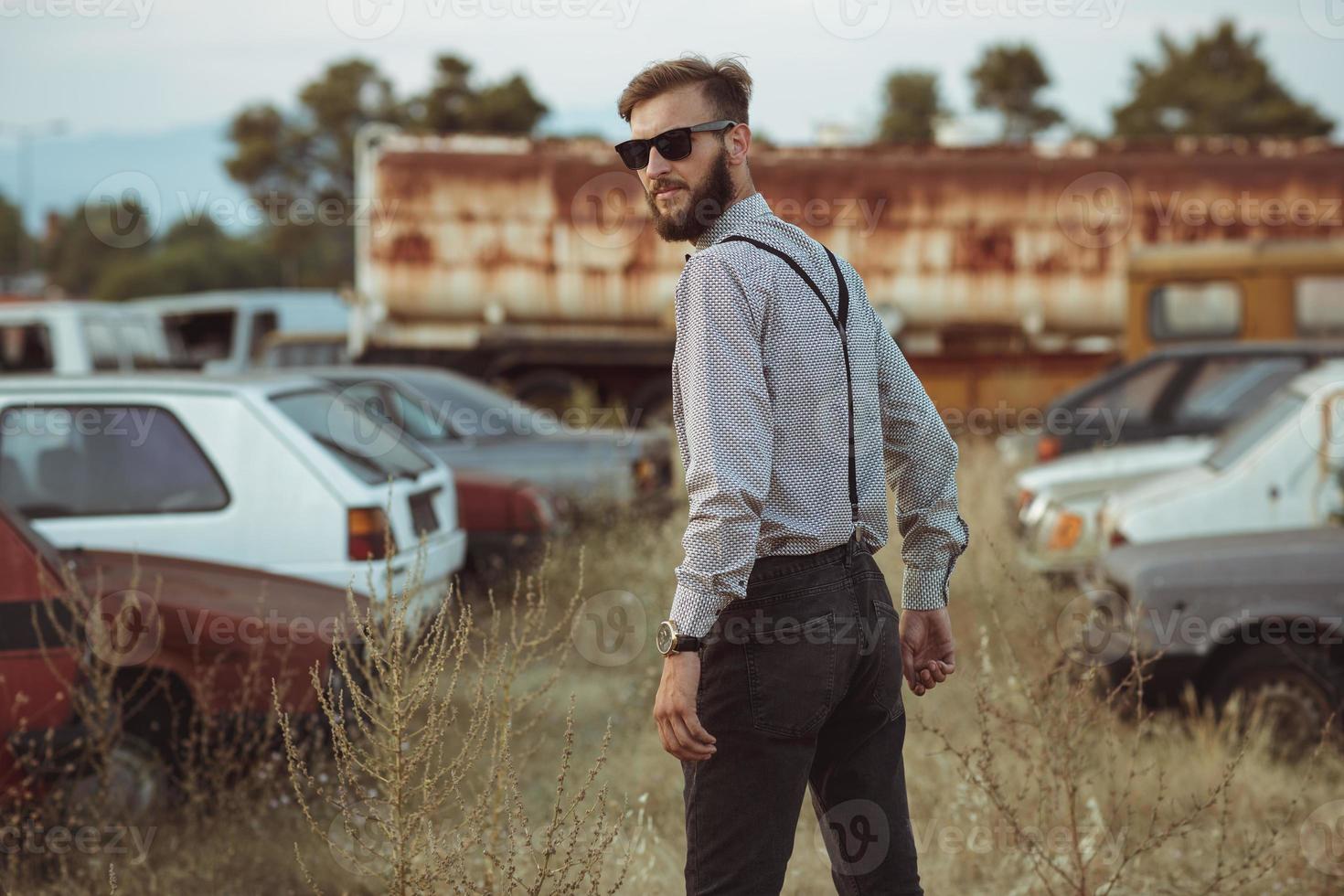 joven hermoso elegante hombre, vistiendo camisa y corbata de moño en el campo de antiguo carros foto