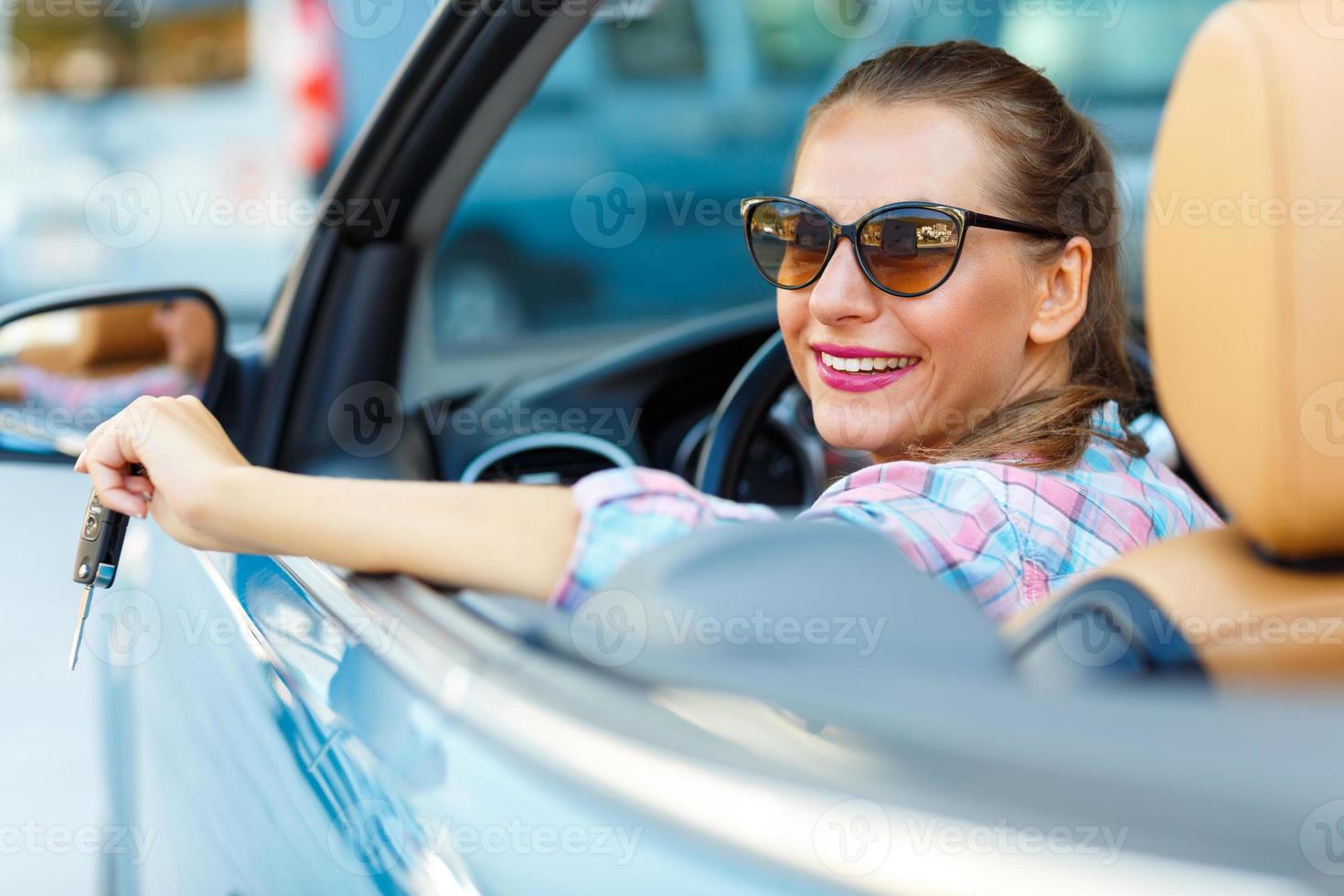 joven bonito mujer en Gafas de sol sentado en un convertible coche con el llaves en mano foto