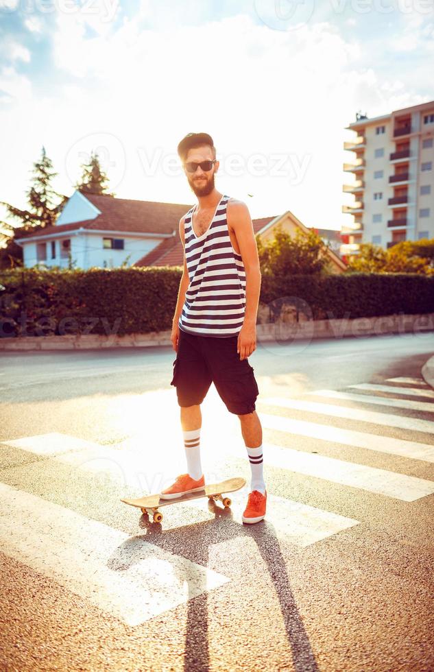 Stylish man in sunglasses with a skateboard on a street in the city at sunset light photo