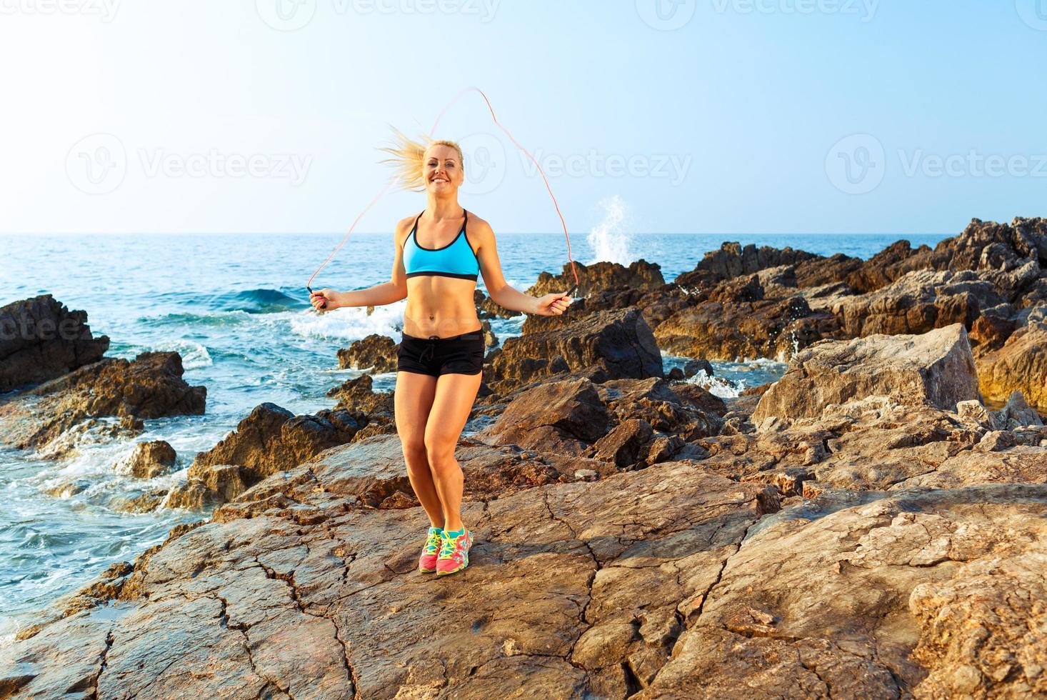 Athlete woman doing sport exercising with the rope on the rocks by the sea photo