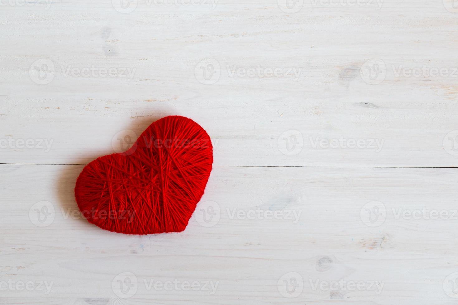 Red heart shape made from wool on white wooden background photo