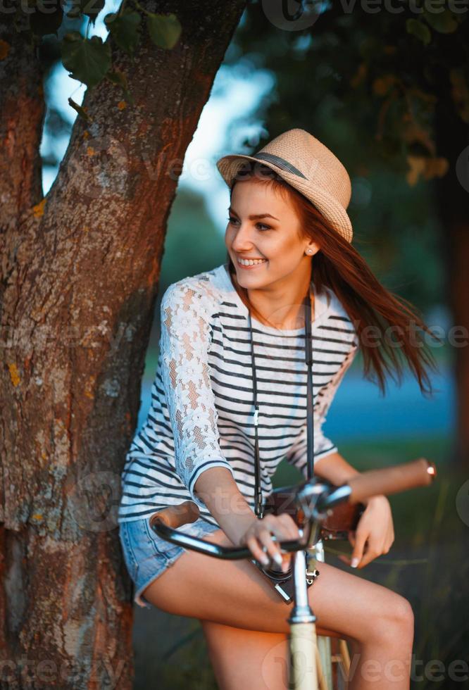 Lovely young woman in a hat with a bicycle outdoors photo