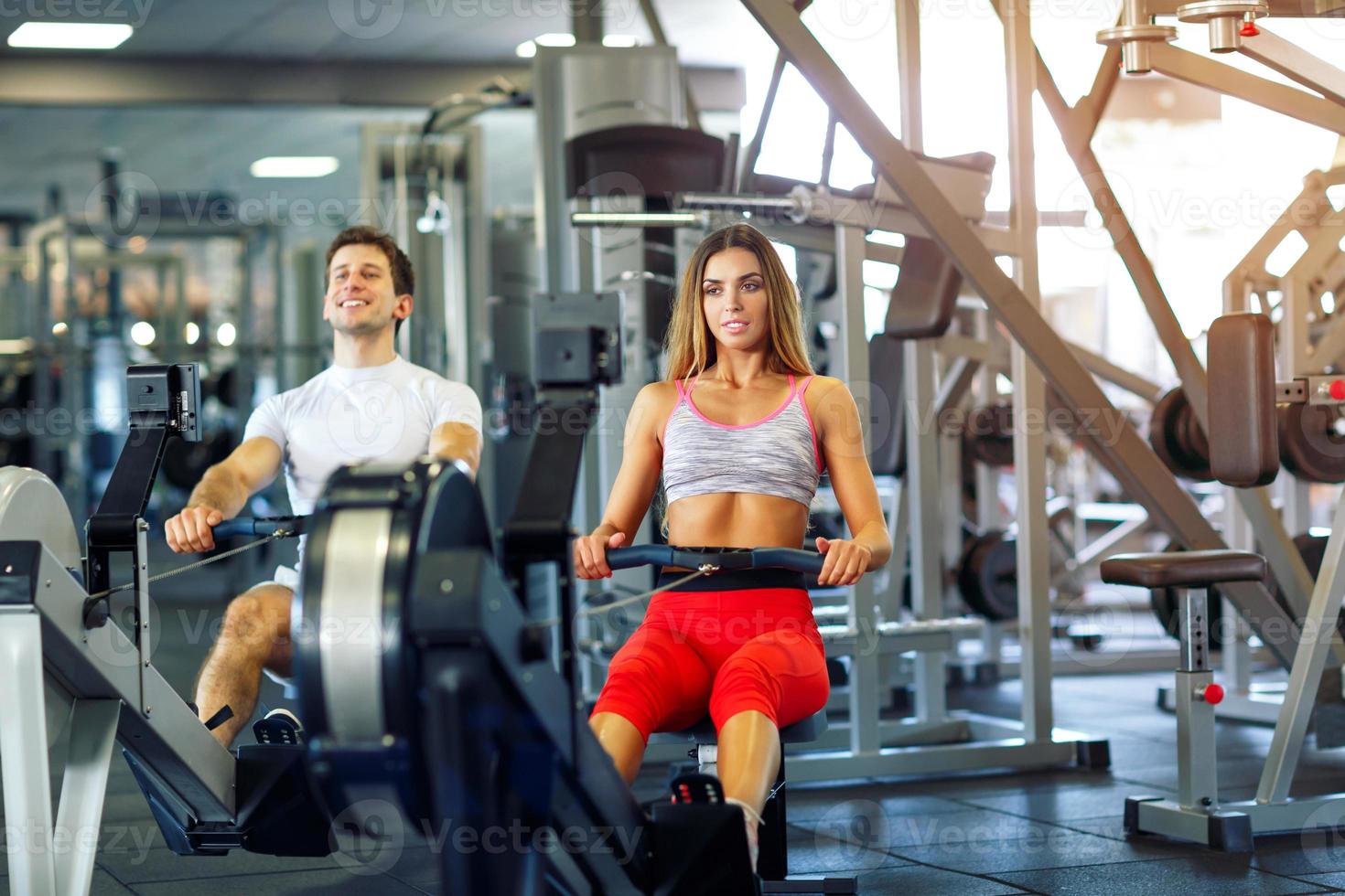 Athletic man and woman training on row machine in gym photo