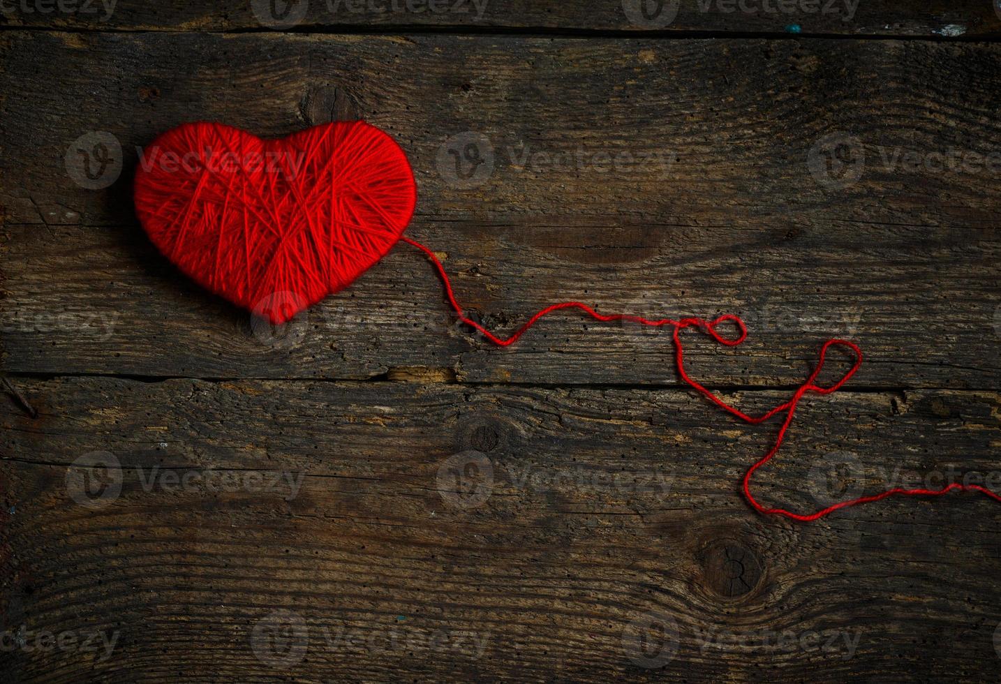 Red heart shape made from wool on old shabby wooden background photo