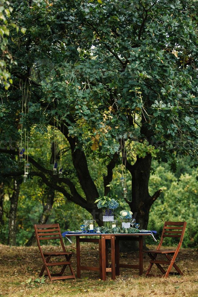 decoración. detalles. Boda decoraciones en el de madera mesa en el bosque allí es un flor arreglo con azul, blanco, verde flores y verdor, velas, estatuillas, vasos, cuchillería. foto de cerca