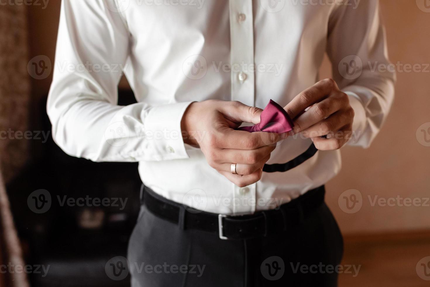 Grooms morning preparation, handsome groom getting dressed and preparing for the wedding, holding a red butterfly in his hands. Wedding day photo
