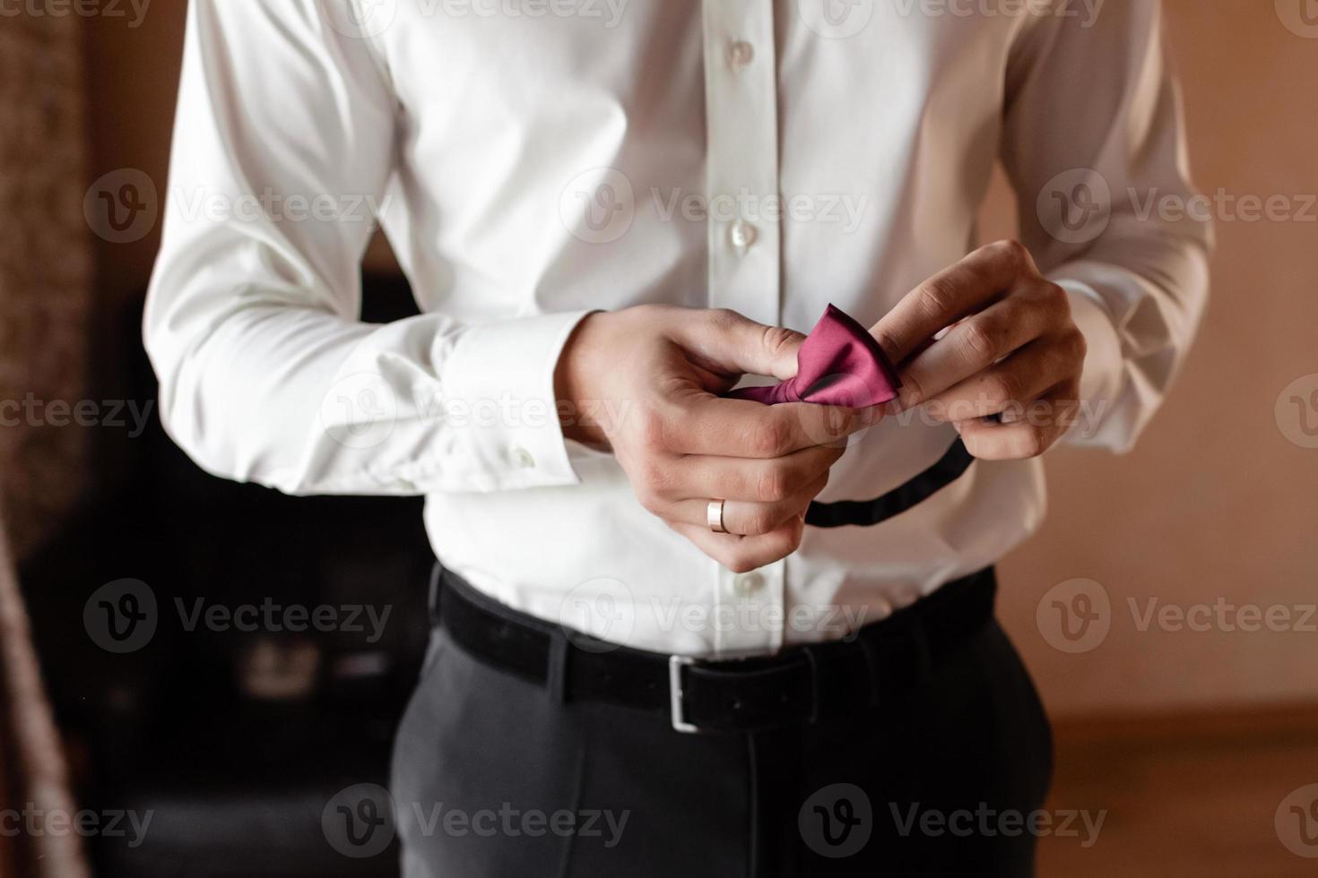 novios Mañana preparación, hermoso novio consiguiendo vestido y preparando para el boda, participación un rojo mariposa en su manos. Boda día foto