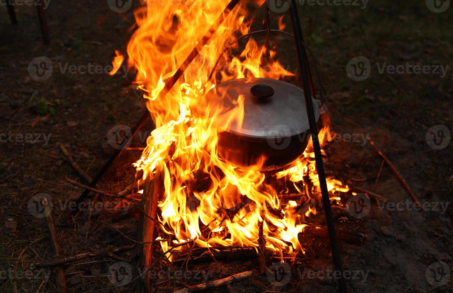 Cooking outdoors in field conditions. Cauldron on a fire in the forest. Cooking at the stake while traveling. Tripod with a bowler hat on a fire on picnic. Conceptual travel, trekking and adventure photo