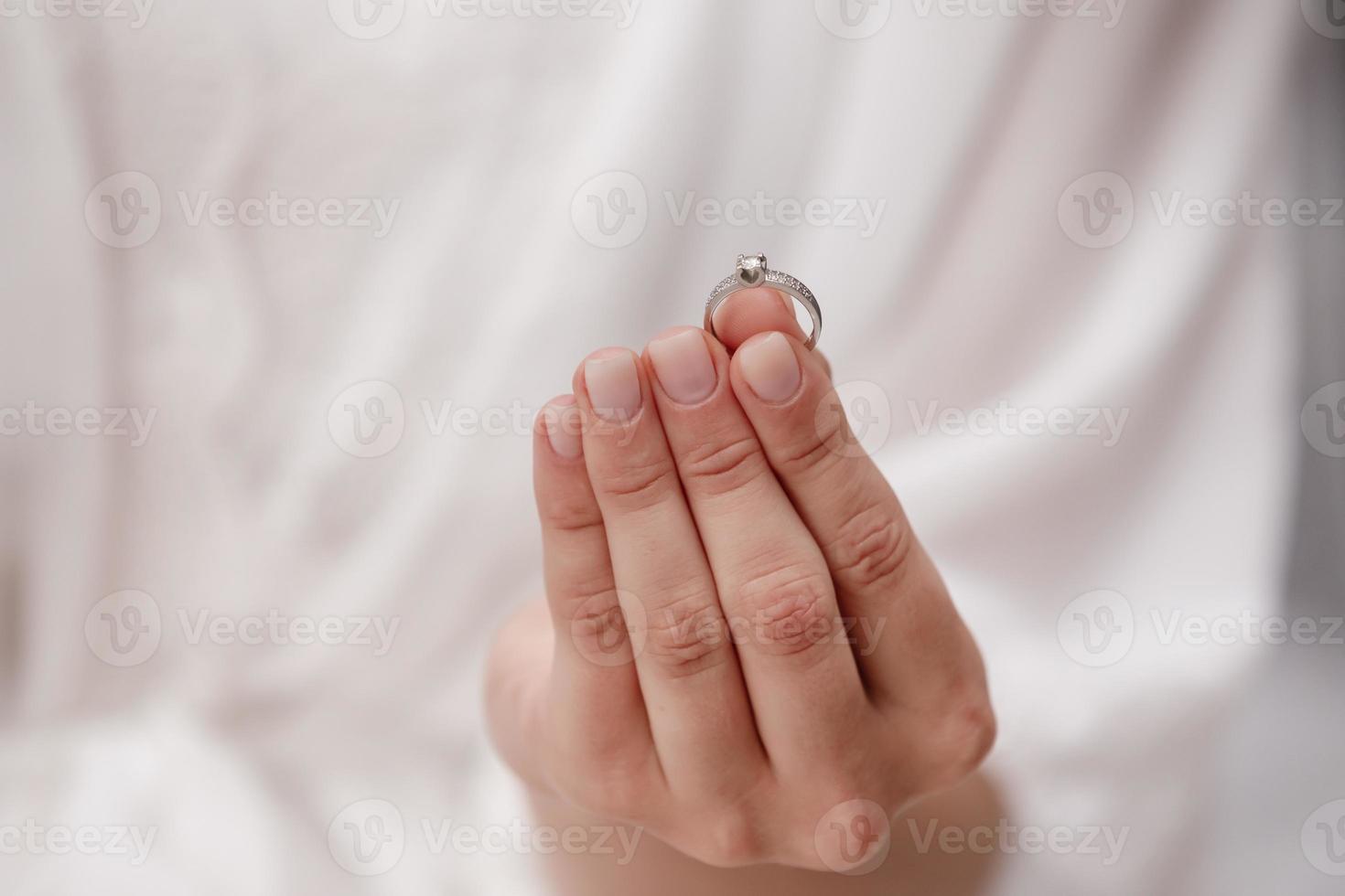 female hand holding wedding ring made of white gold and diamonds on a white background. Luxury expensive proposal ring. Bride in wedding day. photo