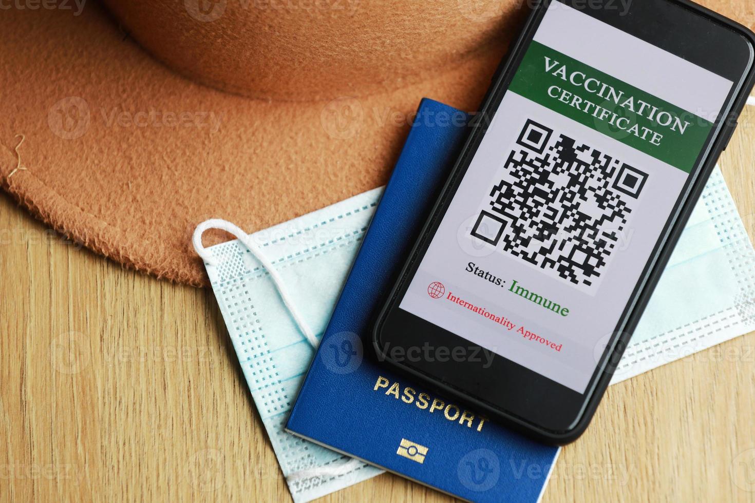 New normal concept. Close up view of a smartphone with an immune digital health passport. In the wooden background, protective mask, hat and passport. photo