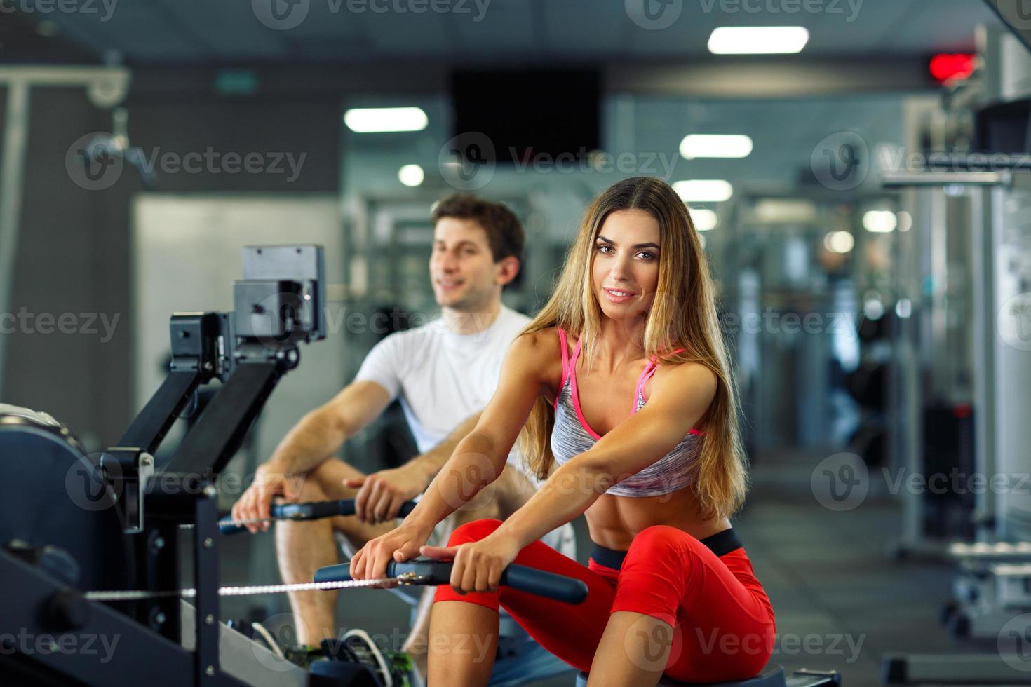 Athletic man and woman doing workout on rowing simulator in crossfit gym photo