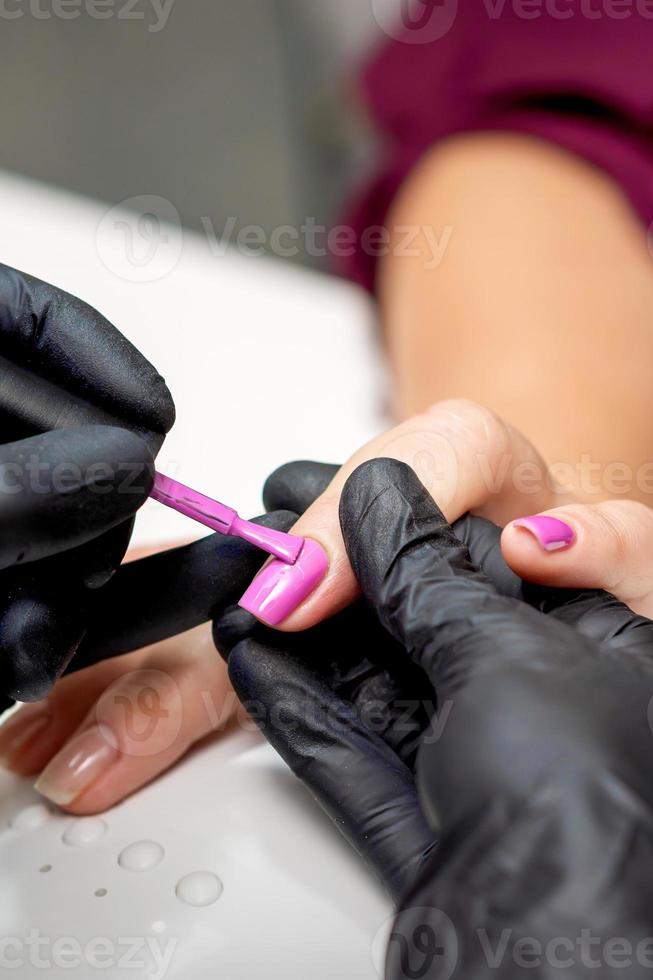 Manicure master applying pink nail polish photo