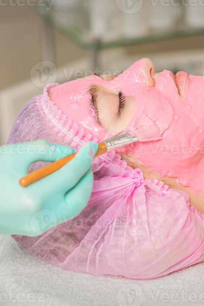 Cosmetologist applying pink alginic mask photo