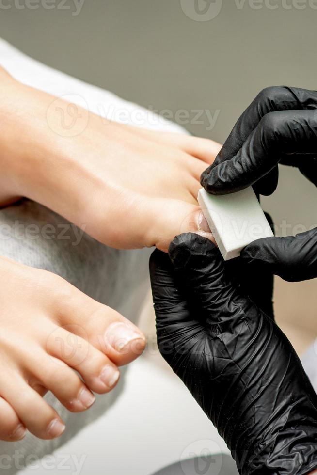 Pedicurist buffing toenail of woman photo