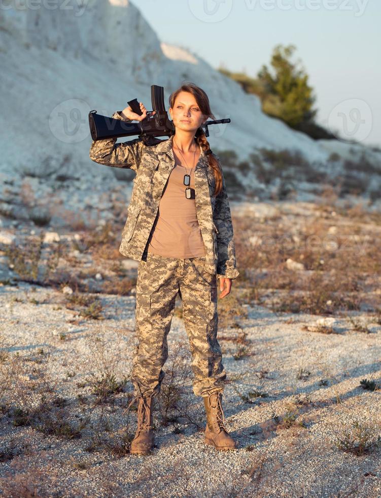 joven hembra soldado vestido en un camuflaje con un pistola en el ubicación foto