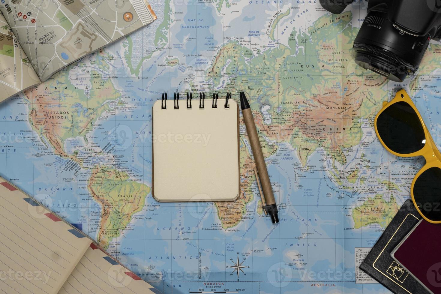 Travel Flat lay of an empty notebook, sunglasses, passport, camera over a world map photo