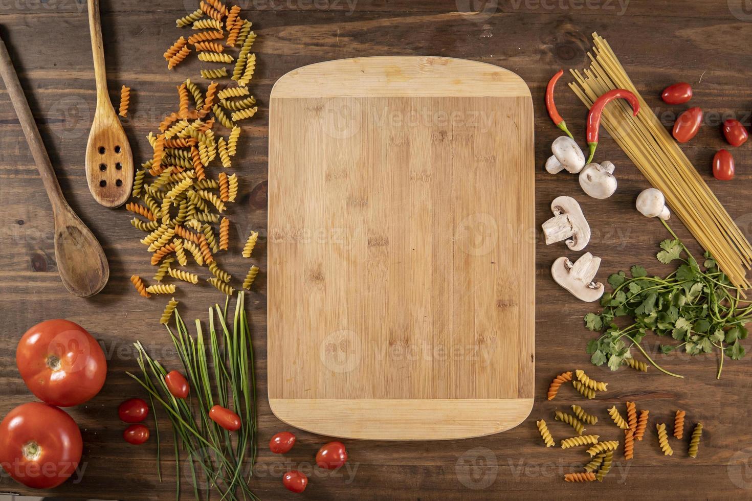 Flat lay of vegetables and food and a chopping table over a wooden table photo