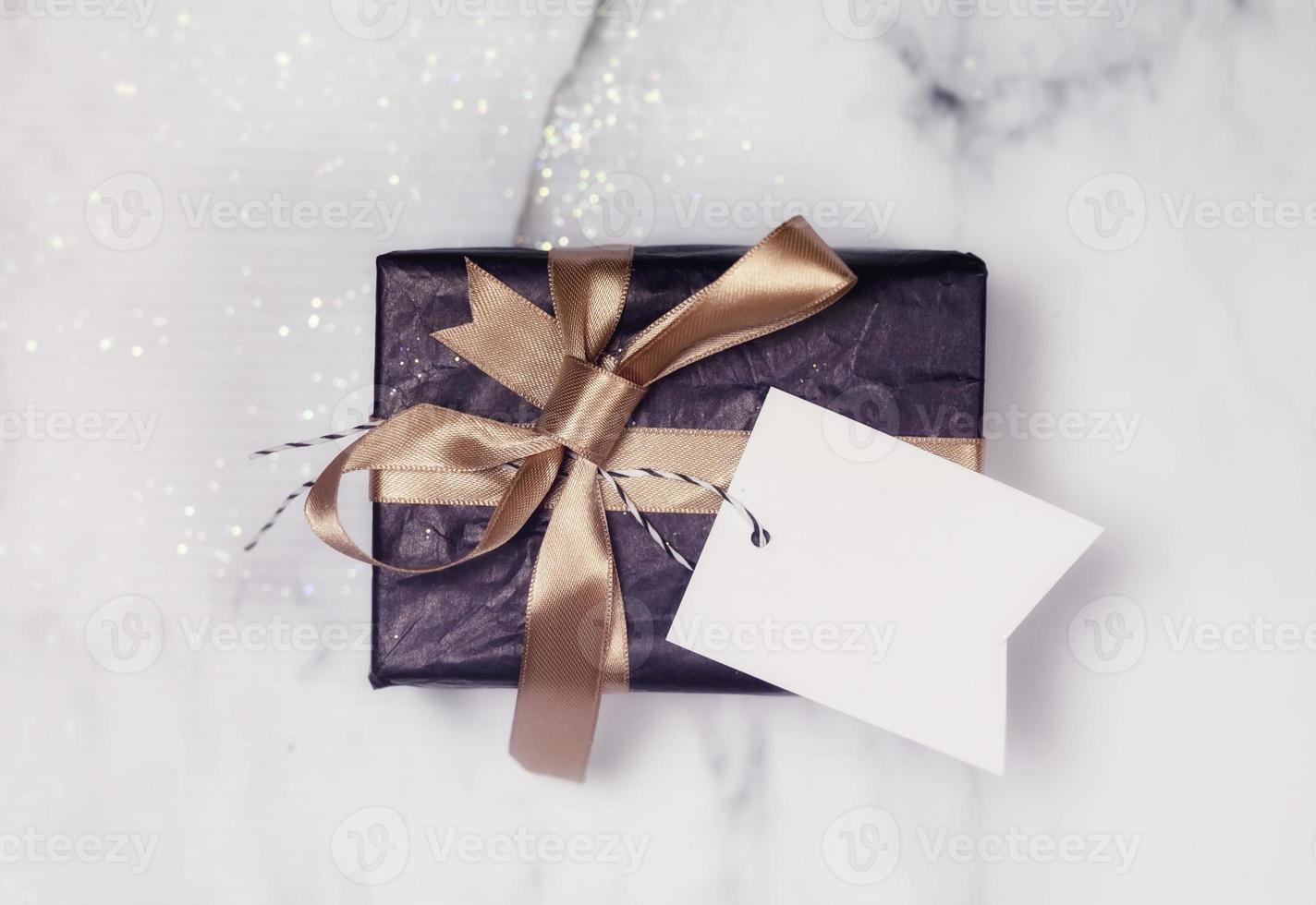 Black Gift With Gold Bow And Empty white Card on a white and black marble table with a bit of glitter photo