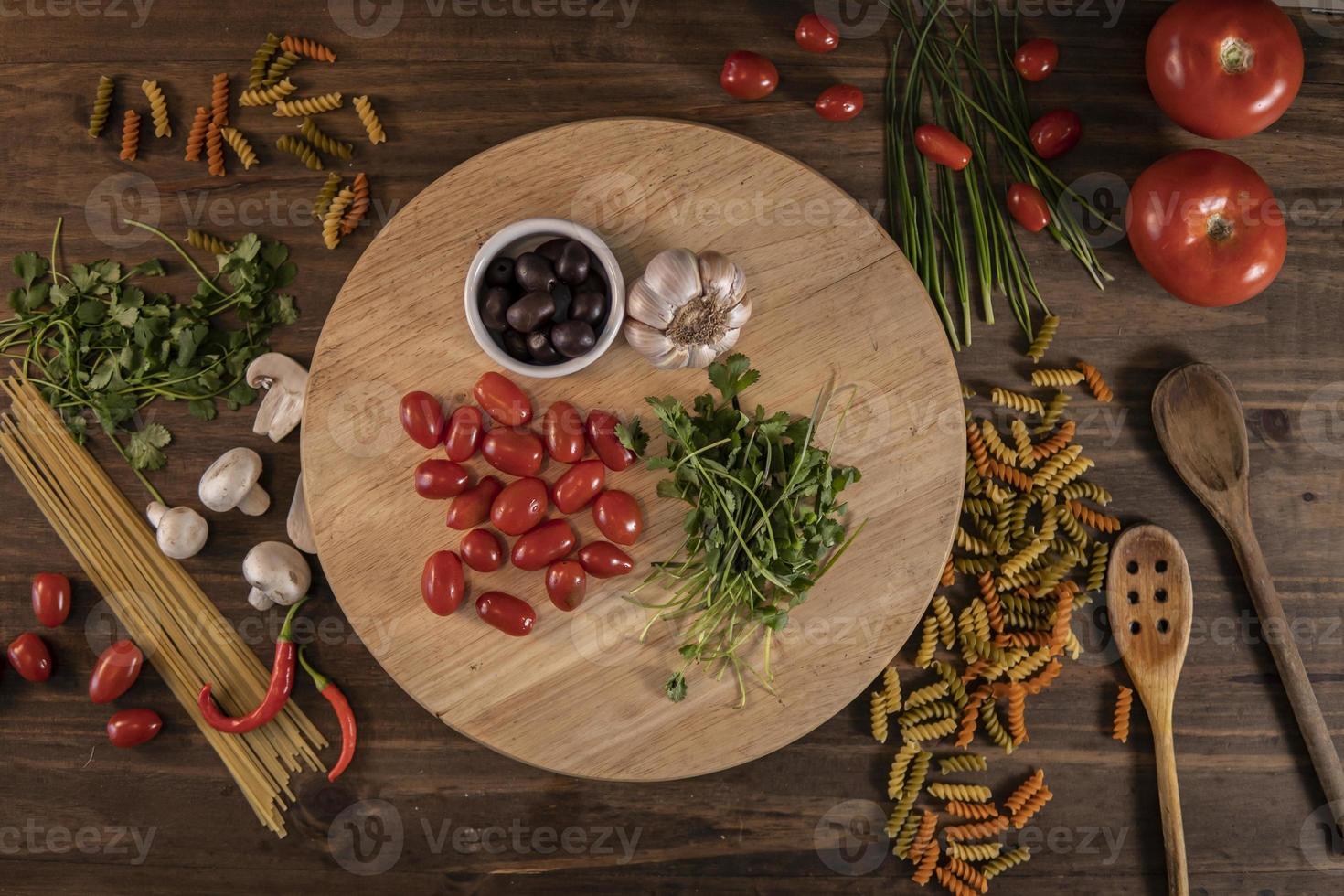 Flat lay of vegetables and pasta and a chopping board over a wooden table photo