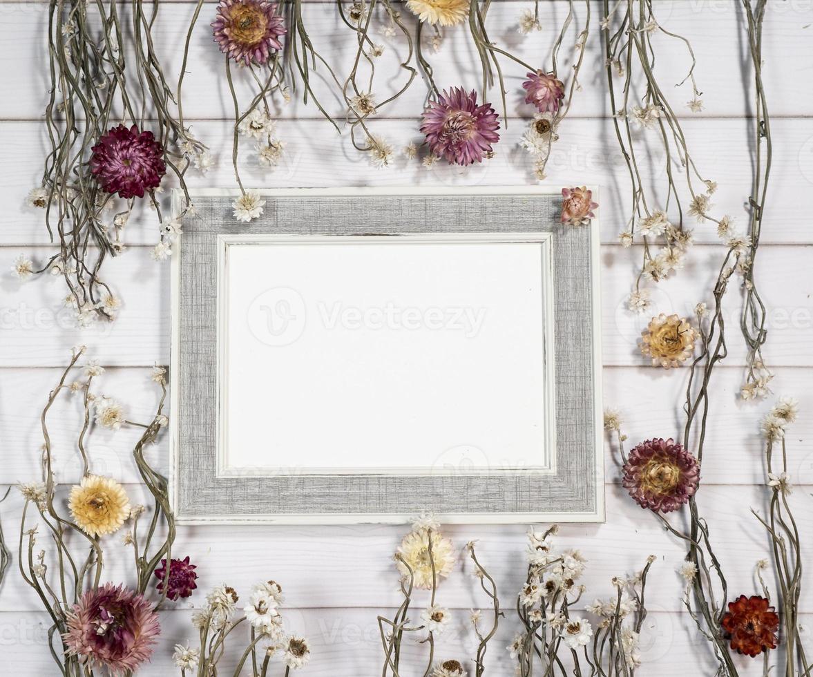 Top view of empty photo frame with dry colorful flowers over a white wooden table