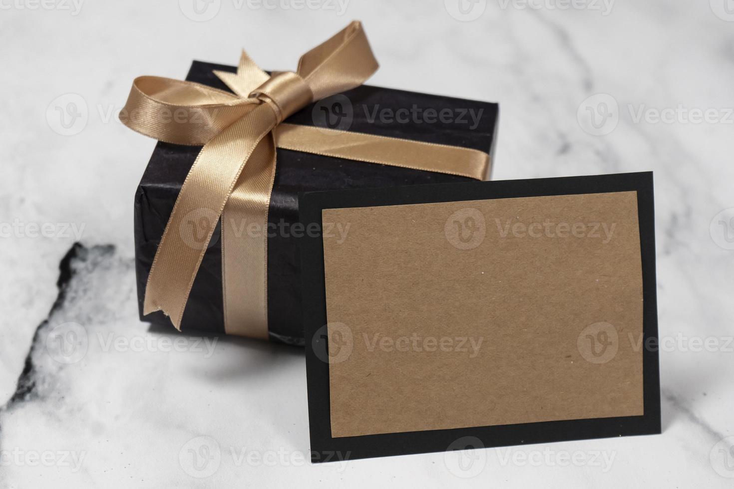 Black gift box with a golden ribbon With an empty Card on a white and black marble tabl photo